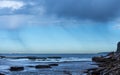 Coastal Rain falling over the ocean against blue sky with seaside rock ledge