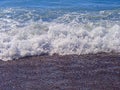 Coastline, shallow water. Sea surf. A foaming wave rolls ashore. Abstract background texture wet sea pebbles. Royalty Free Stock Photo