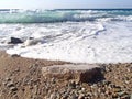 Coastline, shallow water. Sea surf. A foaming wave rolls ashore. Abstract background texture wet sea pebbles. Royalty Free Stock Photo