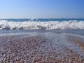 Coastline, shallow water. Sea surf. A foaming wave rolls ashore. Abstract background texture wet sea pebbles. Royalty Free Stock Photo