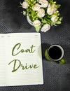 Coat Drive concept on notebook or agenda with cup of coffee and flower`s pot. Royalty Free Stock Photo