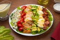 Cobb salad in a white salad bowl with ingredients on a brown background. Royalty Free Stock Photo