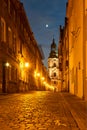 A cobbled street with a baroque belfry of a historic monastery at night