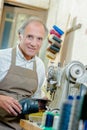 Cobbler holding shoe stood next to sewing machine