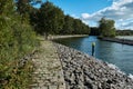 Cobblestone path near a waterway leading from a lake to a marina with a forest to the left.