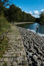 Cobblestone path near a waterway leading from a lake to a marina with a forest to the left. Vertical shot Royalty Free Stock Photo