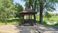 A cobblestone and wood-paved path approaches the wooden gazebo, and next to it stands a metal pole with a lantern. Behind them, ol