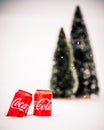 Coca Cola cans with small Christmas trees in the background