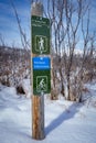 E-bike friendly sign and walking trail sign on a wooden post at a trailhead after a snowfall at Glenbow Ranch Provincial Park.