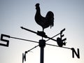 A cockerel weathervane shown in silhouette against a pale blue-grey sky