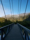 Beautiful early morning view of a suspension bridge with blue sky, light clouds, mountains, trees and fog in the background Royalty Free Stock Photo
