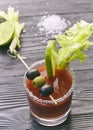 Cocktail Bloody Mary with lime and celery, salt and snacks in a glass on a black wooden table. vertical view of a cocktail