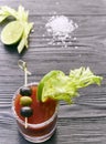 Cocktail Bloody Mary with lime and celery, salt and snacks in a glass on a black wooden table. vertical view of a cocktail