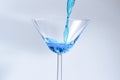 Cocktail with blue liquid in glass. Glass with blue water pouring with liquid with splashes and drops. Martini glass filling with Royalty Free Stock Photo