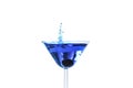 Cocktail with blue liquid in glass. Glass with blue water pouring with liquid with splashes and drops. Martini glass filling with Royalty Free Stock Photo