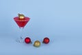 Cocktail glass with red cocktail and Christmas bauble balls on blue background Royalty Free Stock Photo