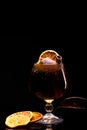 Cocktail with ice cube, lemon and cinnamon stick in a glass on a black background