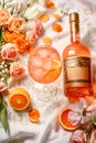 A cocktail with ice cubes in apricot and a bottle of alcohol with a decorative label and text space on a tablecloth with roses and