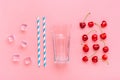 Cocktail ingredients - paper tubes with blue, white stripes, ice cubes, cherry, glass cup isolated on pink background Flat lay Top Royalty Free Stock Photo