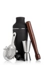 Cocktail set with black shaker and wooden muddler and measuring jigger with strainer on white