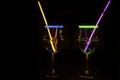 Cocktail wine glass filled with illuminated refreshing juicy liquid and colorful straw with black background for nightlife