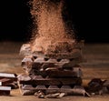 Cocoa powder sprinkles on a stack of broken dark chocolate on a wooden table, black background