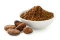 Cocoa powder in a white ceramic bowl next to roasted unpeeled cocoa beans isolated on white