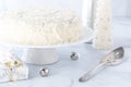 A coconut covered white frosting cake surrounded by white decorations.