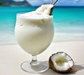 Coconut dream cocktail glass on white sand beach near crystal clear turquoise water against vibrant blue sky. Summer seaside