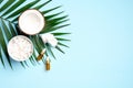 Coconut essential oil on blue background with half of coconut, sliced coconut in bowl and tropical palm leaf. Flat lay, top view. Royalty Free Stock Photo