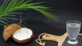 Coconut exotic fruit, two halves of the fruit in the shell, a dark background, a glass of coconut water on the kitchen and