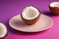 Coconut half in pink plate with nut fruits on violet and purple plain background, abstract food tropical concept