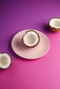 Coconut half in pink plate with nut fruits on violet and purple plain background, abstract food tropical concept