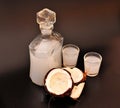 Coconut liqueur in two glasses and a glass decanter, next to a broken nut on a black background Royalty Free Stock Photo