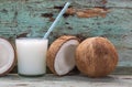 Coconut milk and fresh and halved coconuts on wooden table