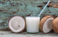 Coconut milk and fresh and halved coconuts on wooden table