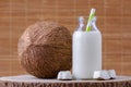 Coconut milk in glass bottle with tubule on natural wooden brown background