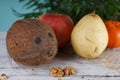 Coconut, pear, apple, tangerine and walnuts on a white wooden table next to a palm tree