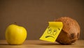 Coconut with sticky post-it note looks sadly at apple