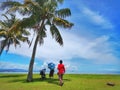 A family outing and coconut tree in the Tanjung Aru Beach, Kota Kinabalu with the beautiful blue sky above on sunny day. Royalty Free Stock Photo