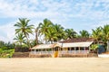 coconut trees on ocean coast near tropical shack or open cafe on beach with sunbeds Royalty Free Stock Photo