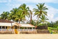 coconut trees on ocean coast near tropical shack or open cafe on beach with sunbeds Royalty Free Stock Photo