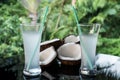 Coconuts and coconut water on the black glass table isolated over blurred palm trees background Royalty Free Stock Photo