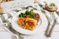 Cod fish fillet on a white plate with brown rice and broccoli. Sliced green onions in a white bowl on a wooden stand. White wood b Royalty Free Stock Photo