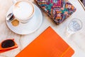 Coffe cappuccino, orange notebook, glass of water and colorful accessories