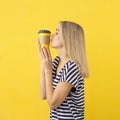 Coffee addict concept. Joyful girl kissing a disposable yellow coffee cup on a yellow background