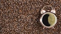 Coffee background of hot black coffee with foam in alarm clock cup on roasted coffee beans background in concept of coffee time Royalty Free Stock Photo