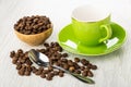 Coffee beans in bowl, scattered coffee beans, spoon, empty cup on saucer on wooden table Royalty Free Stock Photo