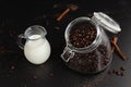 Coffee beans in a glass jar and jug of milk with cinnamon on black background Royalty Free Stock Photo