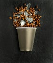 Coffee beans with ice in a paper Cup on a black concrete background. Abstraction, imitation of iced coffee.